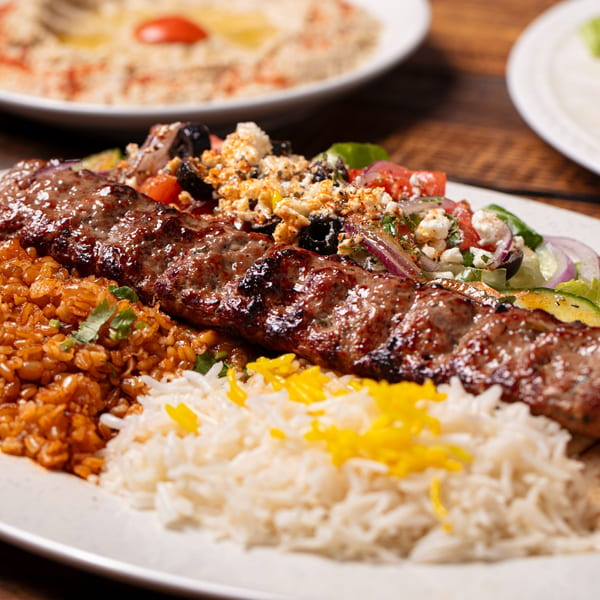 Grilled Mediterranean kebab with rice, bulgur, and a fresh Greek salad topped with feta cheese.