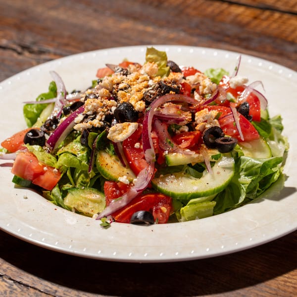 A vibrant Mediterranean salad with lettuce, tomatoes, cucumbers, red onion, olives, and feta cheese.