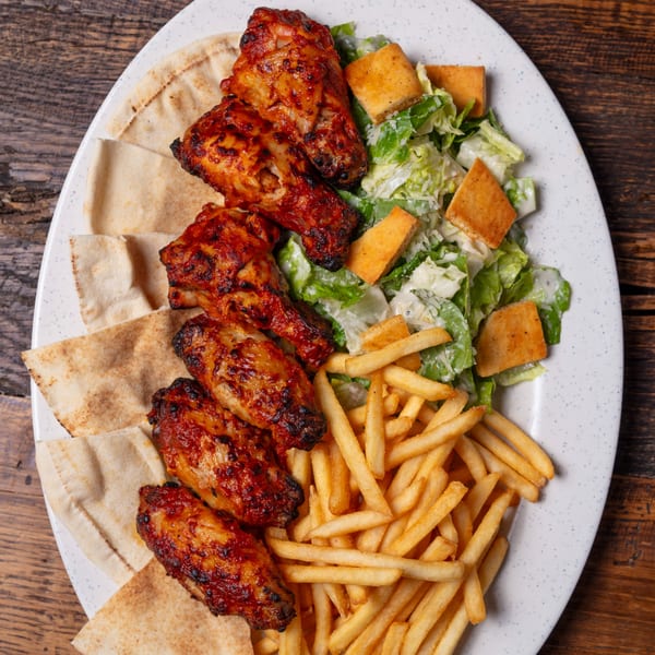 Oliver Pepper's grilled chicken wings, pita bread, Caesar salad, and golden french fries on a white plate.