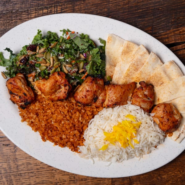 Mediterranean chicken and rice platter with salad and pita bread on a white plate.