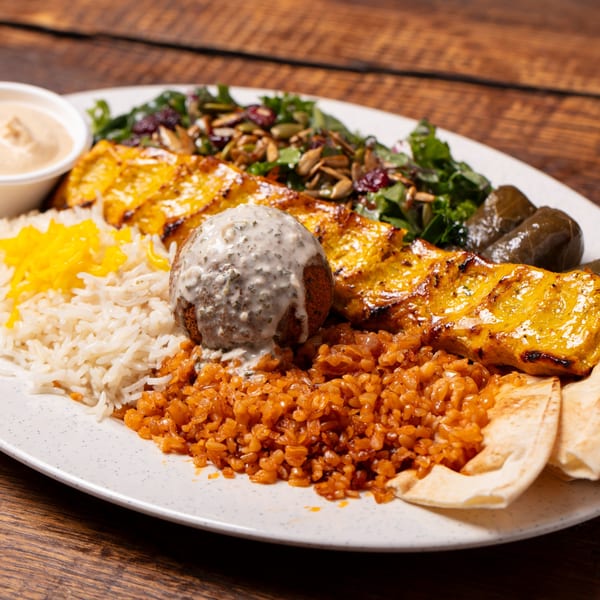 A Mediterranean platter with chicken skewers, falafel, rice, bulgur, salad, stuffed grape leaves, and hummus.