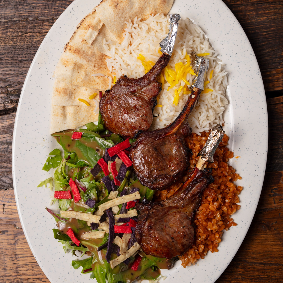 Three lamb chops with rice, salad, and pita bread on a white oval plate.