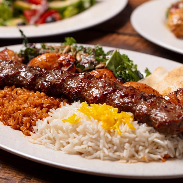 Oliver Pepper's Mediterranean kebab with rice, bulgur, and a side salad on a white plate.