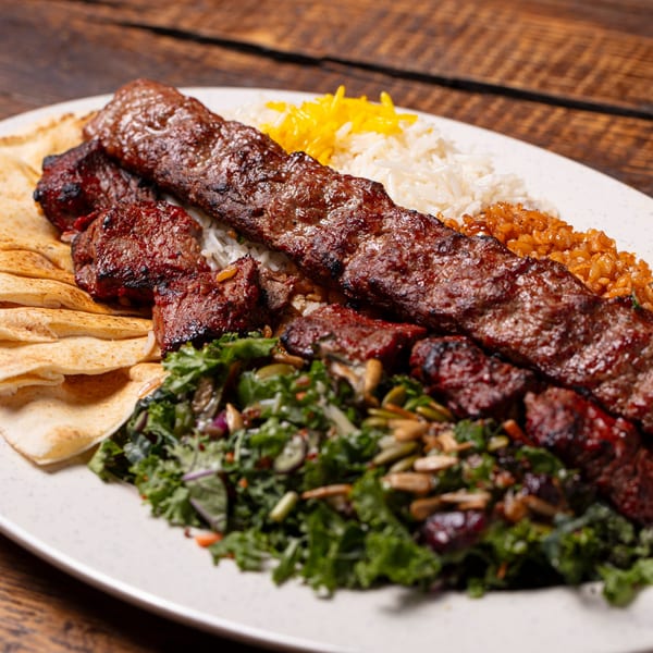 Grilled Mediterranean beef and lamb kebabs with rice, salad, and pita bread on a white plate.
