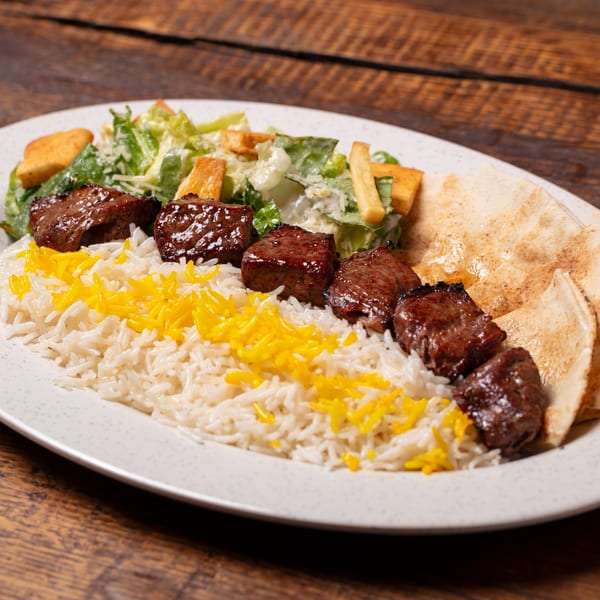 Oliver Pepper's Mediterranean beef skewers with rice, salad, and pita bread on a white plate.