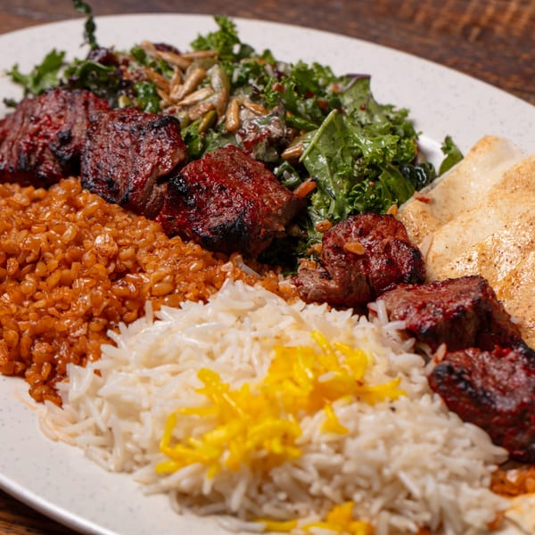 Grilled meat skewers, rice, bulgur, salad with nuts, and flatbread on a white plate.