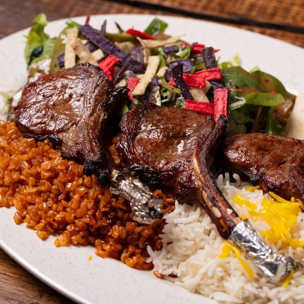Grilled lamb chops with two types of rice and a colorful salad with tortilla strips.