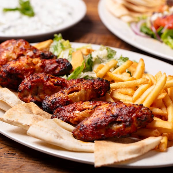 Oliver Pepper's grilled chicken wings with fries, salad, and pita bread on a white plate.